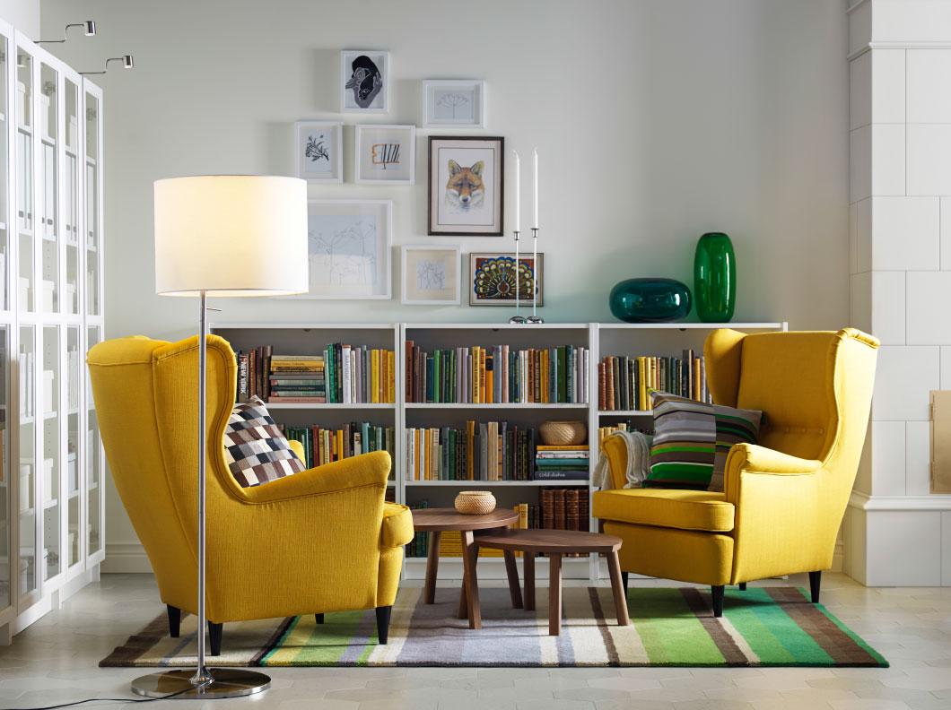 A light living room with two yellow wing chairs, nest of two tables in walnut