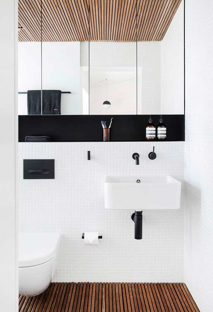A black and white bathroom that follows the trends white tiles, wood on the ceiling and floor, as well as brushed black china